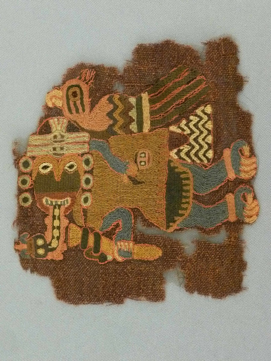 Ser humano con atributos de ave y mono, portando cabeza cortada. Fragmento textil bordado. Paracas Necrópolis, costa sur del Perú, 100 a.C.-200 d.C. Colección Museo Chileno de Arte Precolombino, 0521 (140 x 140 mm)