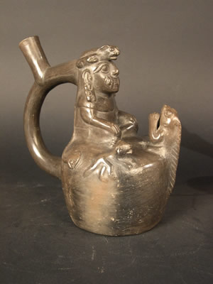 Botella asa-estribo: «Cara Arrugada » con cinturón de serpiente y tocado de felino, acompañado de Iguana y perros. Museo Larco, Lima – Perú f ML013010